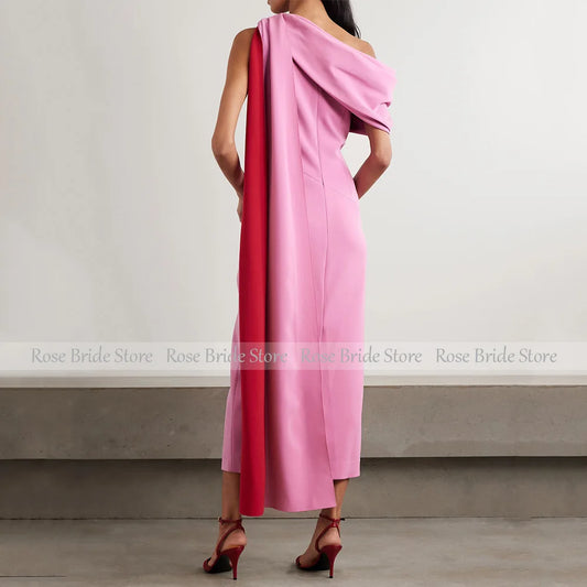 Backview of a pink one-shoulder cape midi dress with a flowing cape.