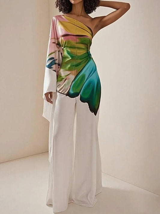 Woman wearing the Celina Studio Printed One-Shoulder Wide-Leg Jumpsuit featuring a colorful botanical print, asymmetrical one-shoulder neckline, and flowing white wide-leg trousers.