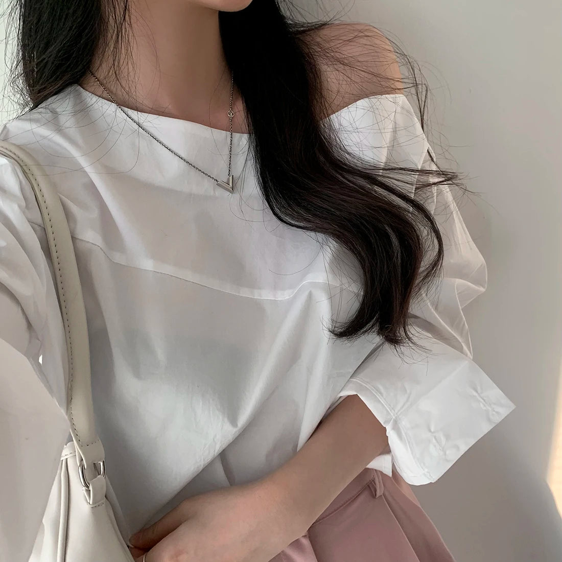 Close-up of a white elegant one-shoulder long sleeve blouse with an asymmetrical neckline.