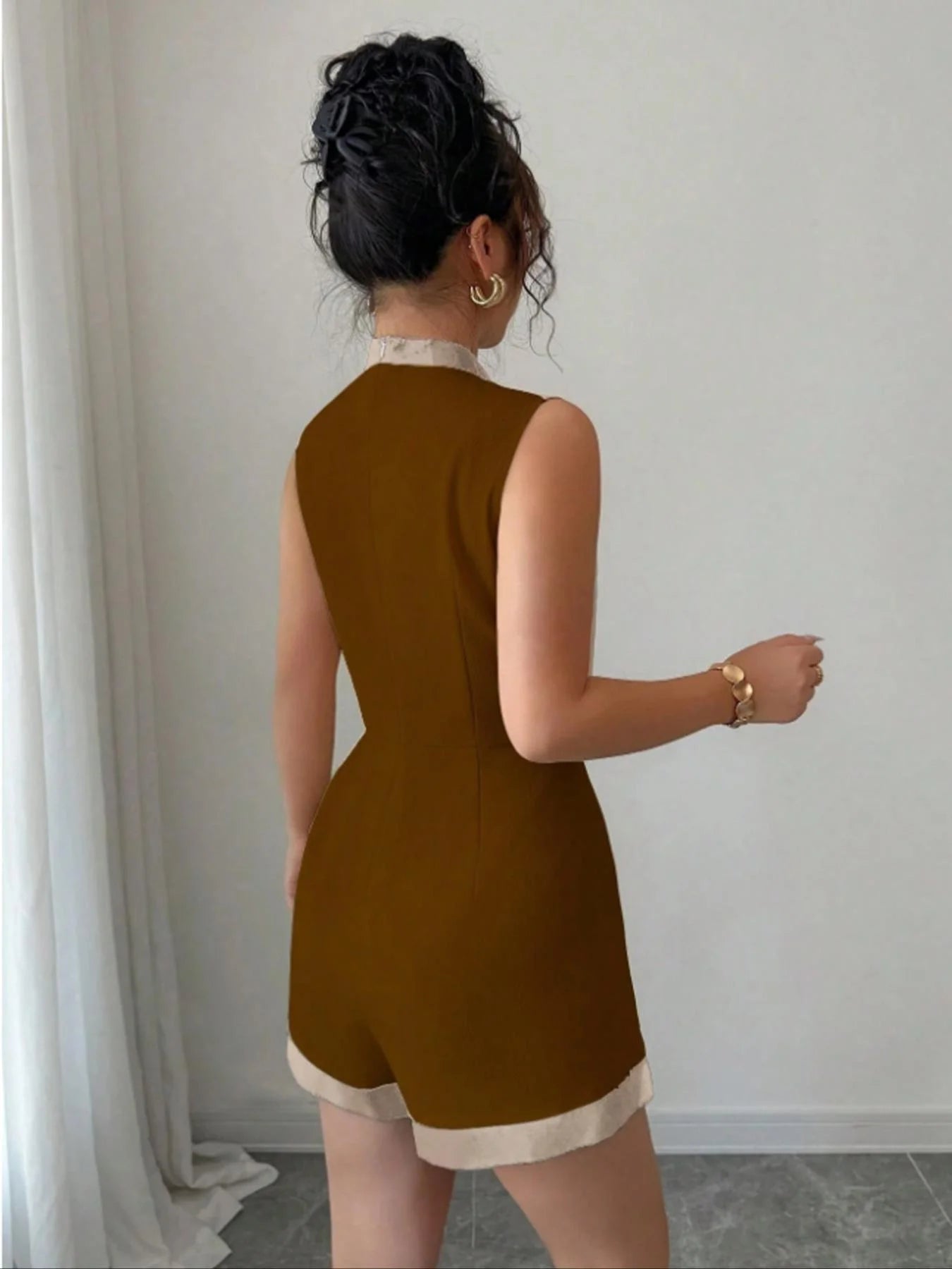 Woman wearing the Celina Studio Brown & Ivory Contrast Trim Sleeveless Romper featuring a modern high neckline, elegant contrast trim, fitted silhouette, and tailored shorts.