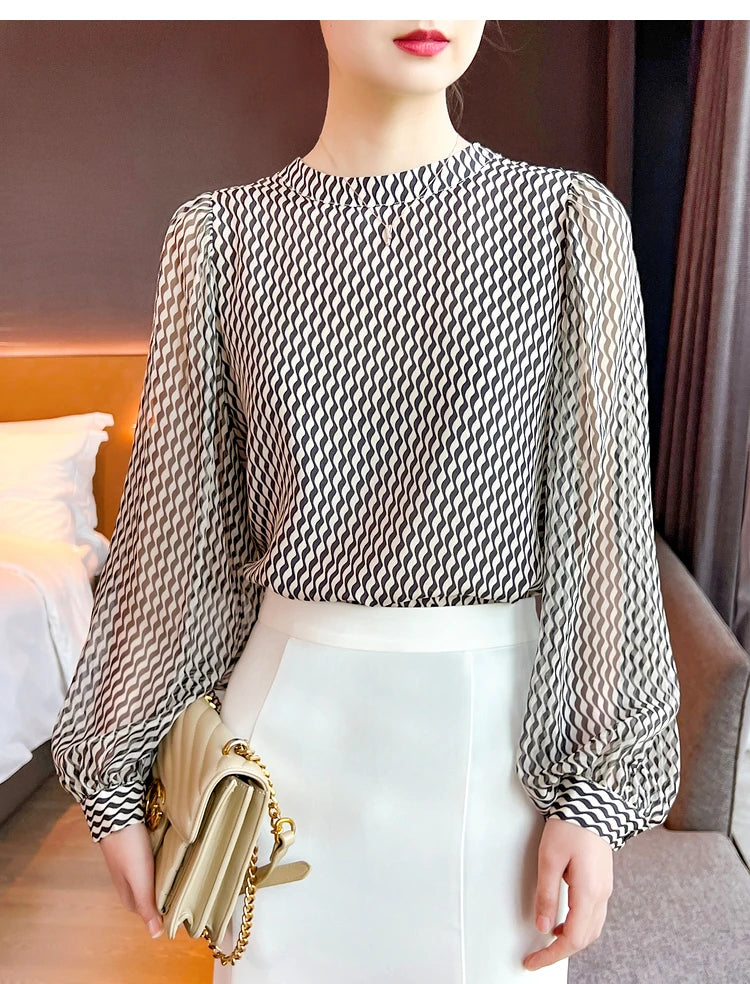Woman wearing a black and beige printed balloon sleeve blouse with a round neckline, paired with a white skirt and a beige handbag.