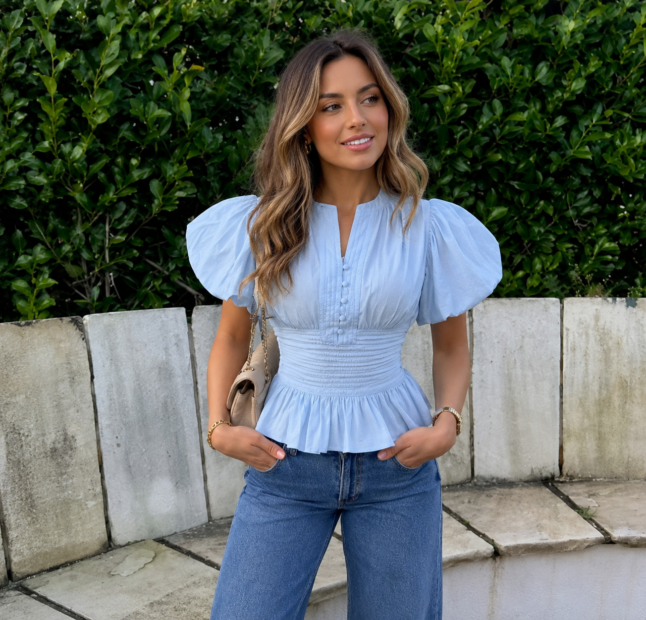 Woman wearing a light blue puff sleeve peplum blouse with blue jeans.