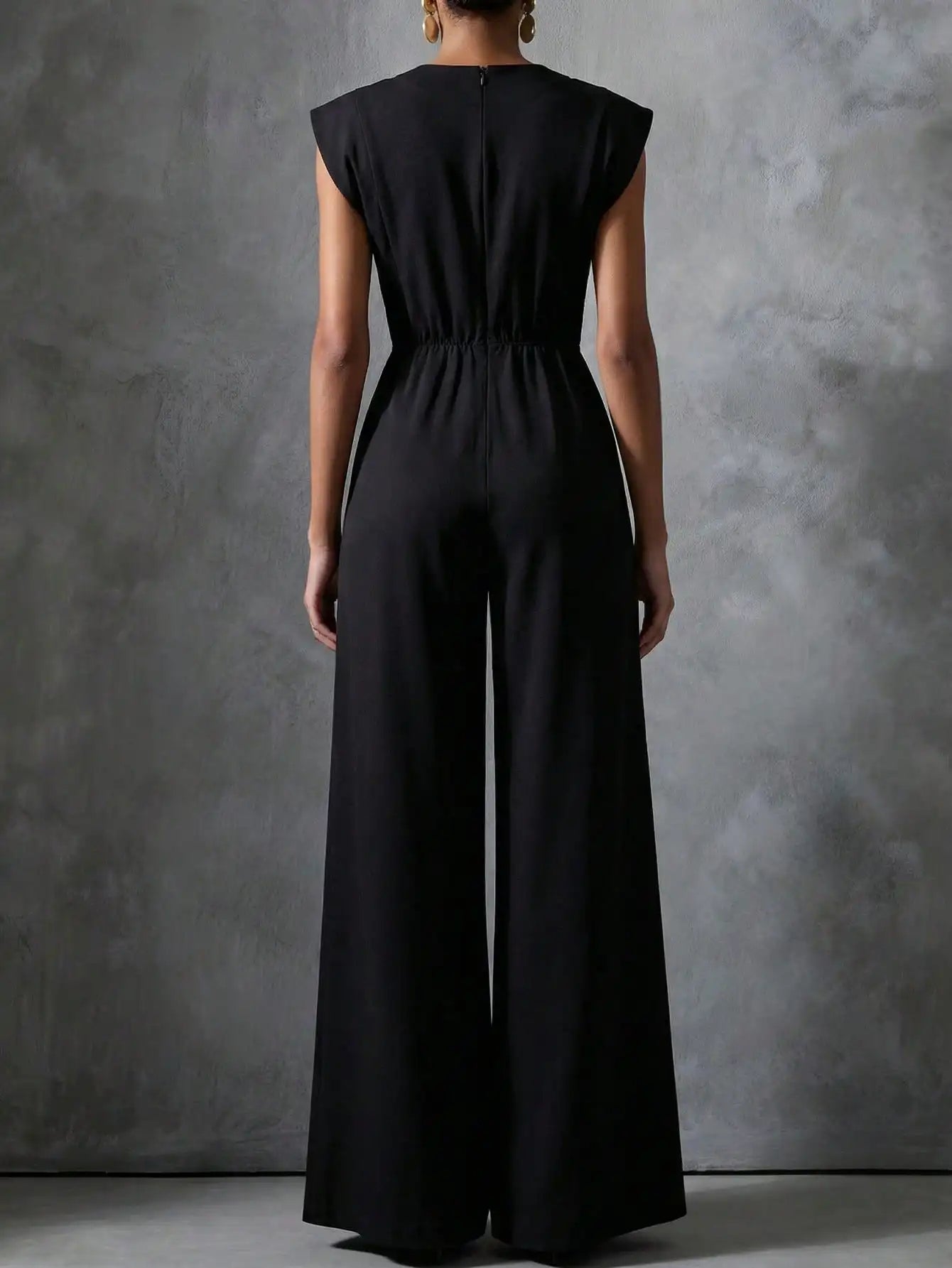 Woman wearing the Celina Studio Noir Luxe Tailored Wide-Leg Jumpsuit in Black with structured shoulders and flowing wide-leg trousers.