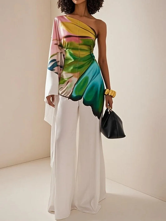Woman wearing the Celina Studio Printed One-Shoulder Wide-Leg Jumpsuit featuring a colorful botanical print, asymmetrical one-shoulder neckline, and flowing white wide-leg trousers.