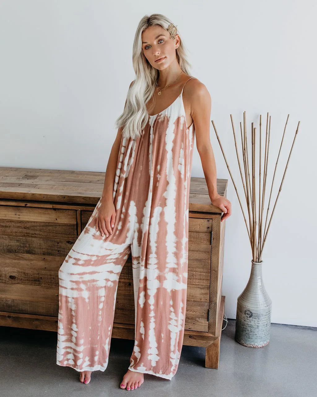Woman wearing the Celina Studio Isla Breeze Printed Wide-Leg Jumpsuit in Blush Pink with adjustable spaghetti straps and a relaxed wide-leg silhouette.